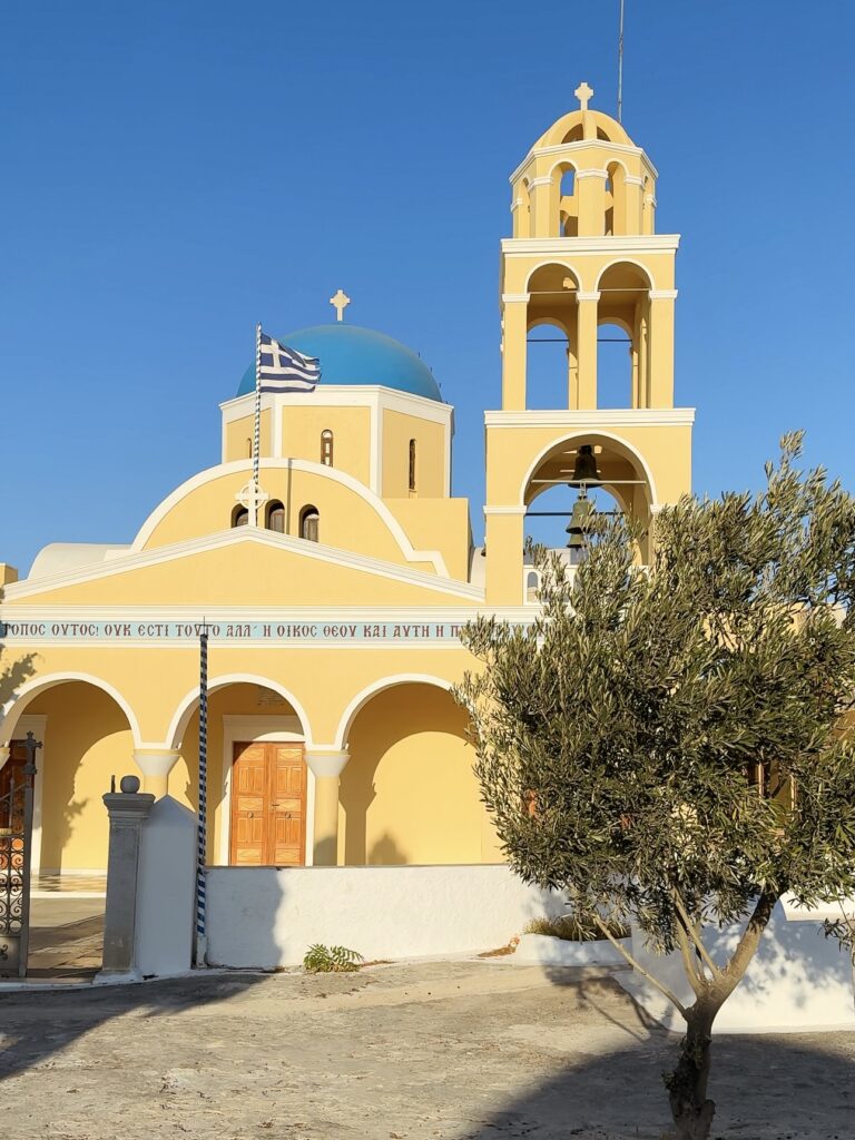 Agios Georgios Church in Oia, featuring classic Cycladic architecture with a blue dome and unique yellow walls