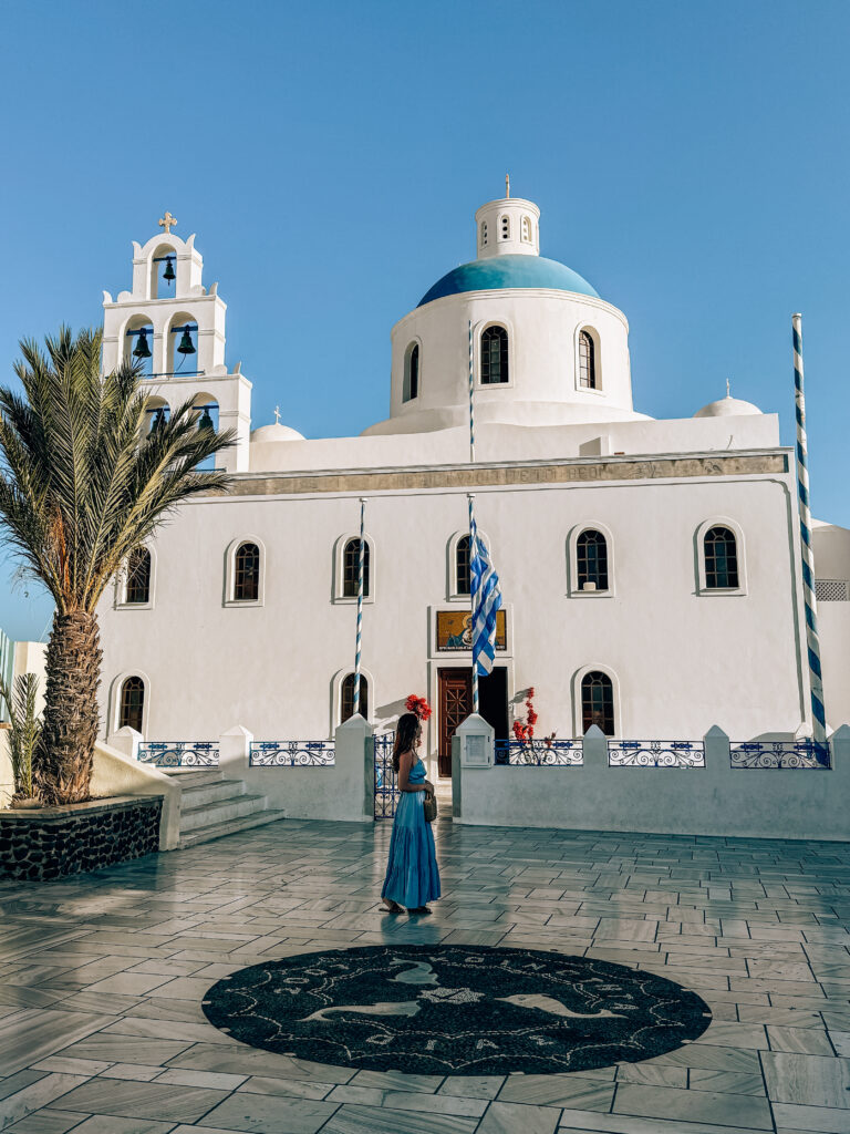 Facade of the Church of Panagia Platsani in Oia, Santorini, with its distinctive blue dome and 6 bells