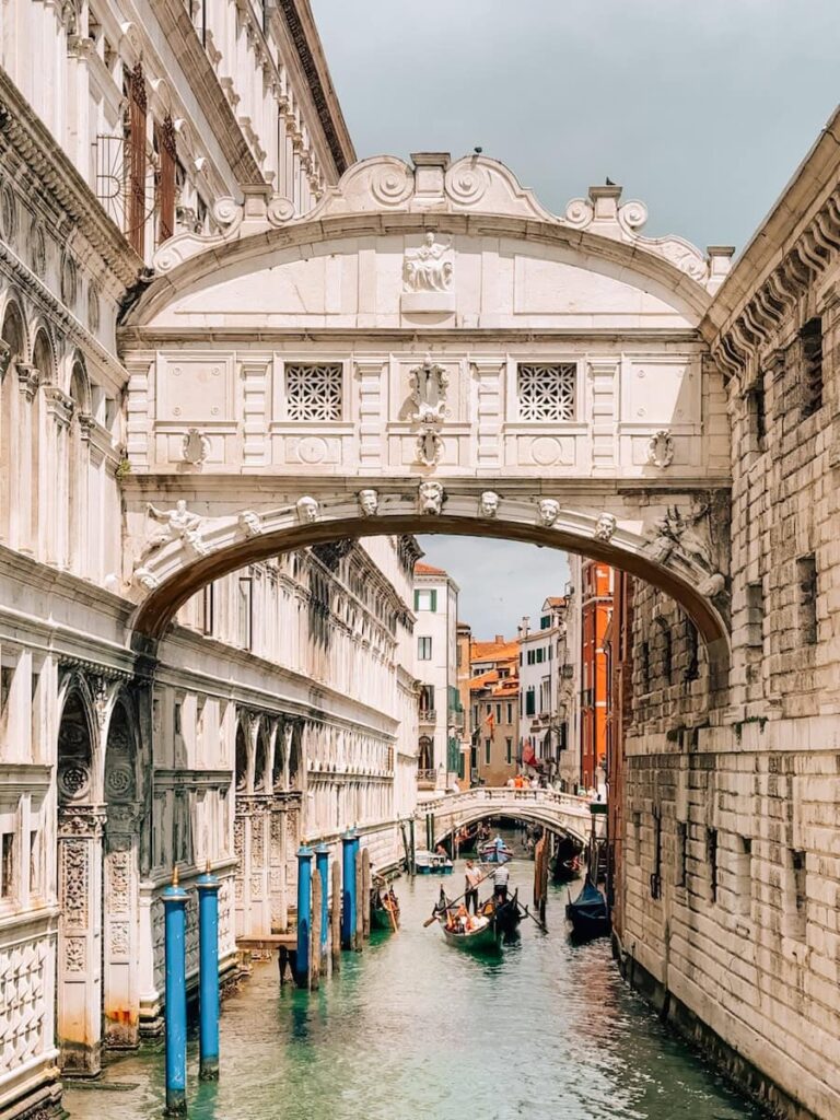 Close up view of the Bridge of Sighs in Venice with gondolas passing through the canal below and ornate white stone architecture surrounding the bridge.
