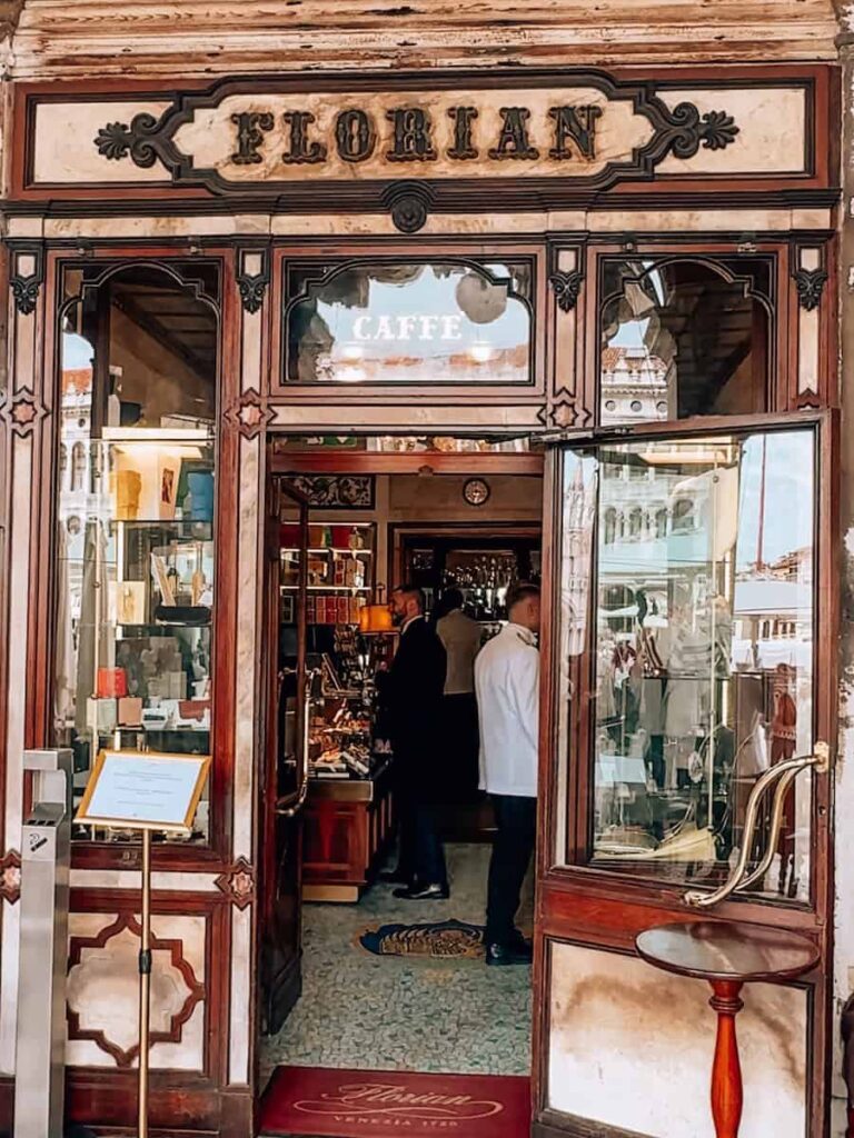 The historic wooden entrance of Caffe Florian with glass display cases and staff inside the cafe on Piazza San Marco.