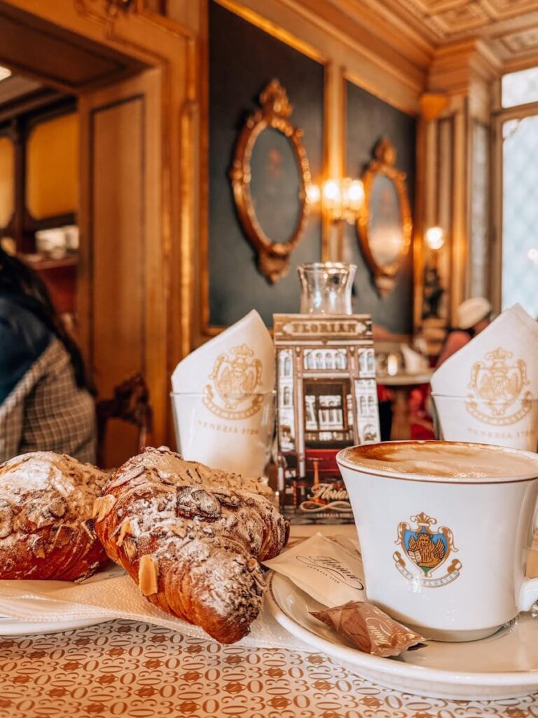 Almond croissants dusted with powdered sugar and a cappuccino served on a marble table inside the historic Caffe Florian in Venice.