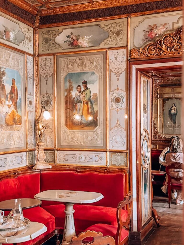 A cozy red velvet corner inside Caffe Florian featuring hand painted wall panels, gilded frames and marble tables.