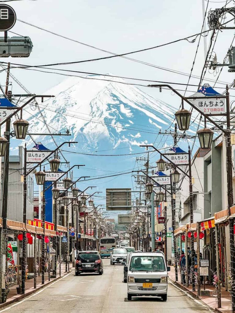 Street view of Honcho Street in Fujiyoshida with Mount Fuji towering in the background, lined with shops and street lamps