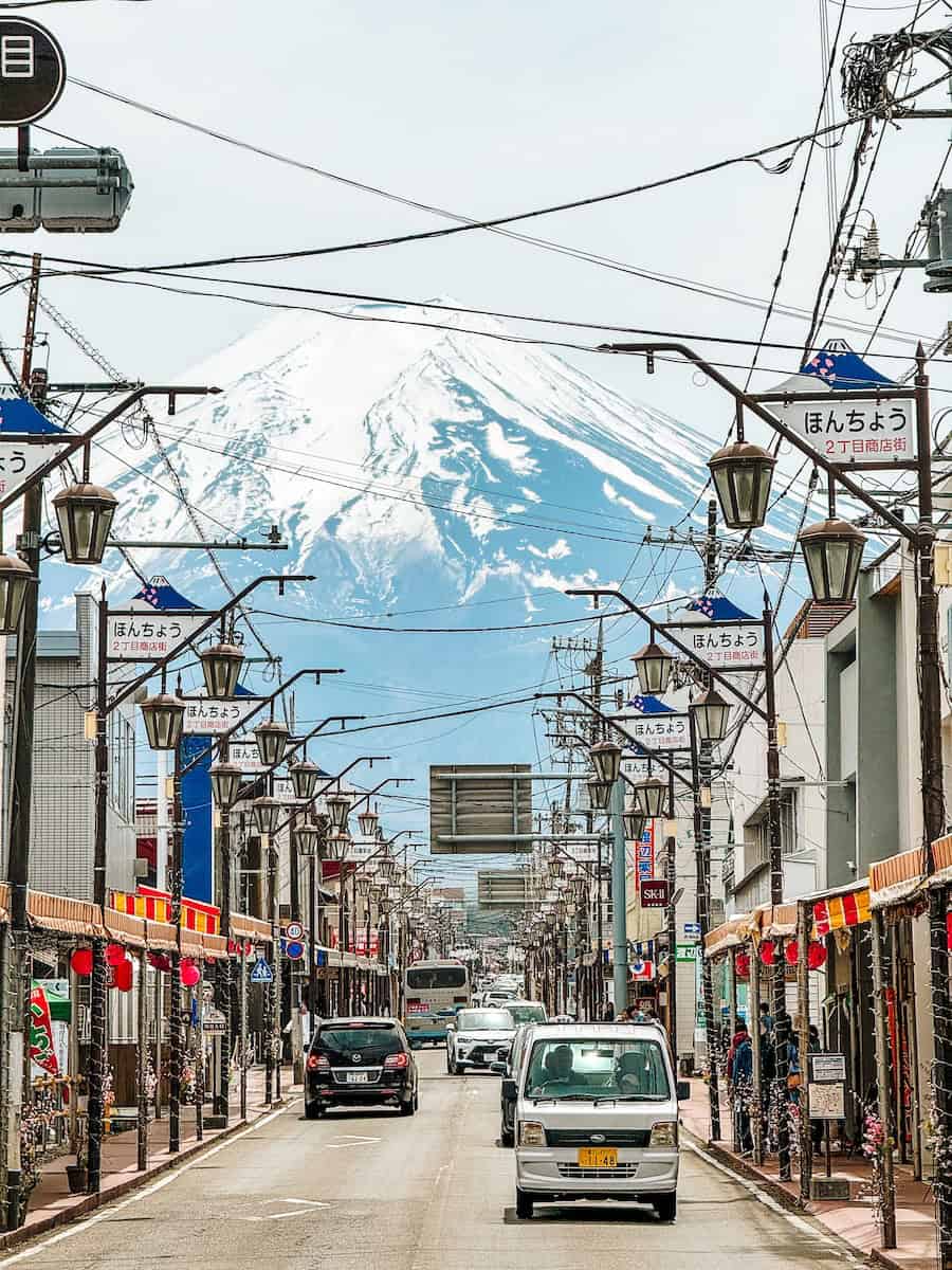Street view of Honcho Street in Fujiyoshida with Mount Fuji towering in the background, lined with shops and street lamps