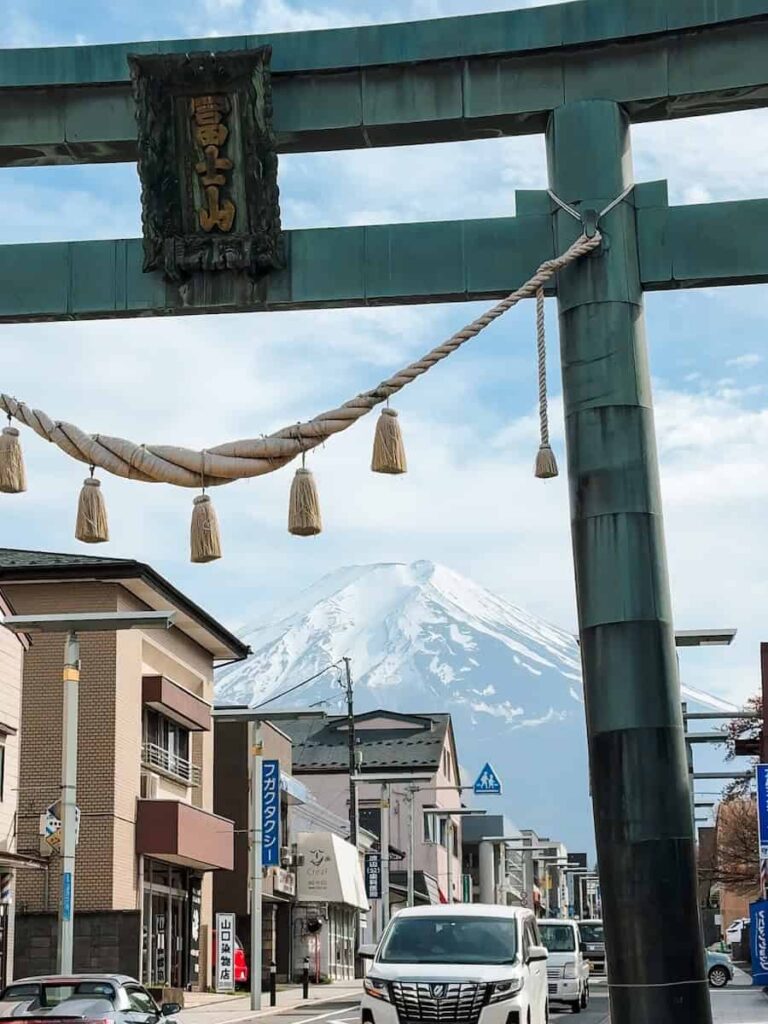 View of Mount Fuji framed by a large torii gate along a street in Fujiyoshida with cars and shops below.