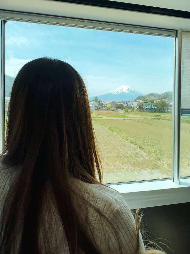 Passenger gazing out the window of the Fuji Excursion train with Mount Fuji visible across the fields.