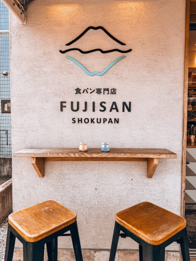 Minimalist café corner at Fujisan Shokupan in Fujiyoshida with two wooden stools and a logo of Mount Fuji on the wall.