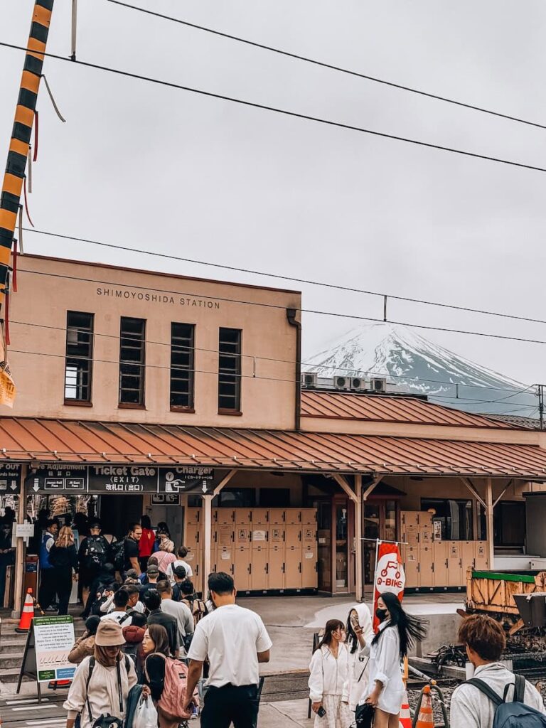 Tourists lining up at Shimoyoshida Station with Mount Fuji partially visible behind the station building.