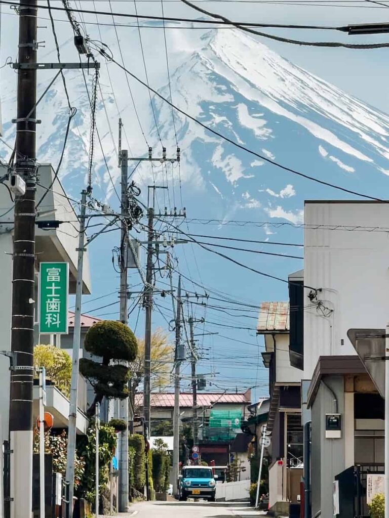Narrow residential street in Shimoyoshida framed by power lines and houses with Mount Fuji rising majestically behind.