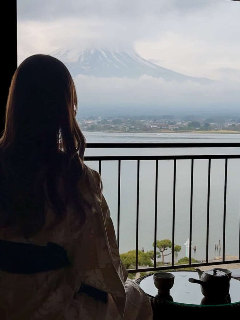 Woman in yukata enjoying tea on a balcony with a serene view of Mount Fuji above Lake Kawaguchi.