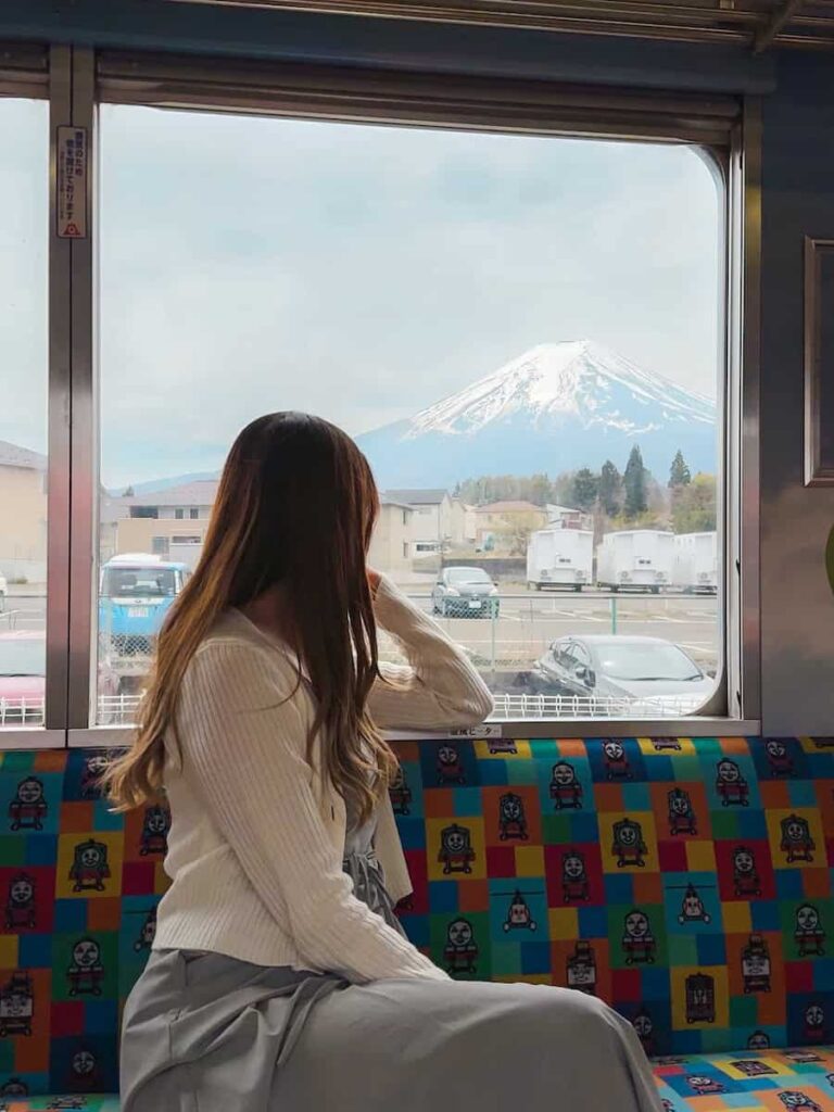 Passenger sitting on a colorful train seat gazing at Mount Fuji through the window of the Fuji Excursion train.