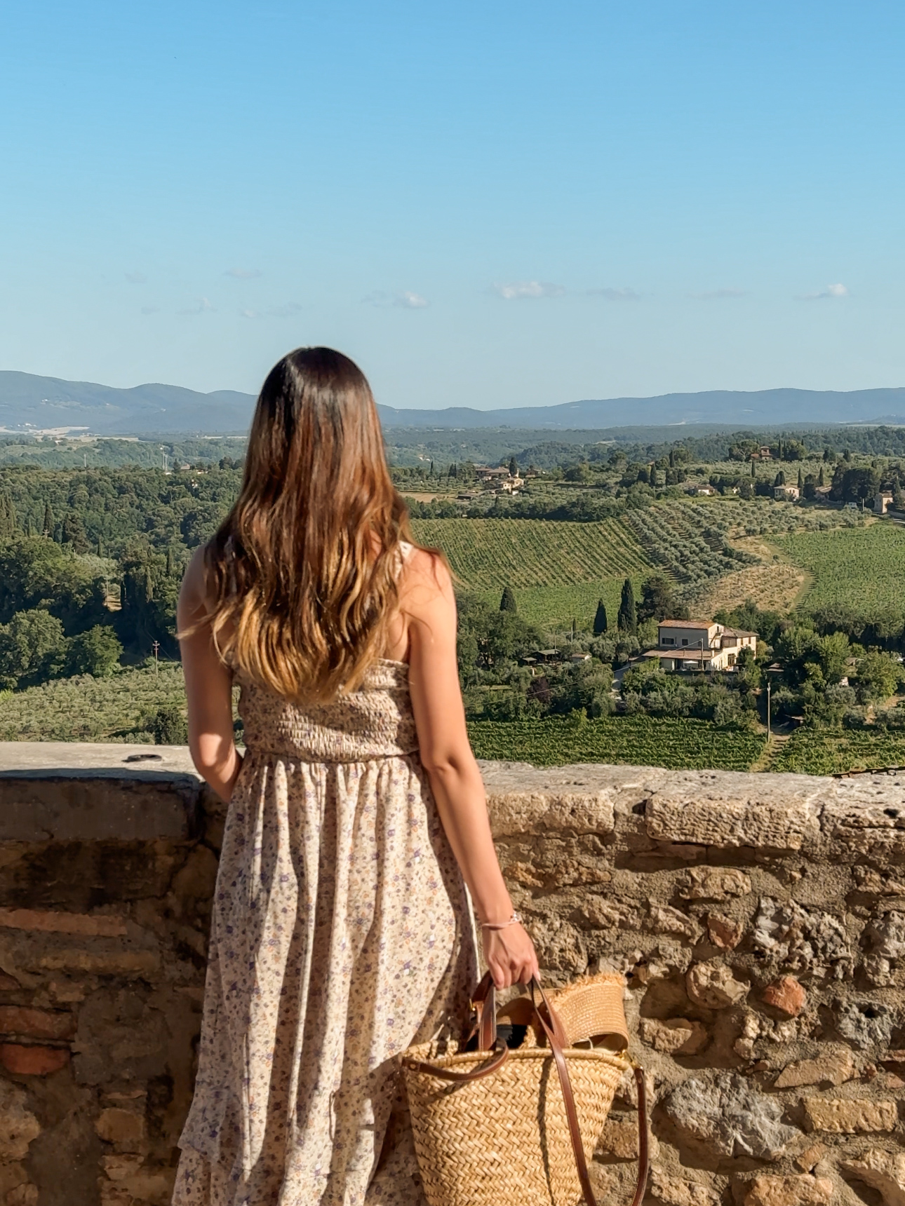A woman overlooking rolling hills of Tuscany from walls of a medieval town during her 7 day tuscany itinerary