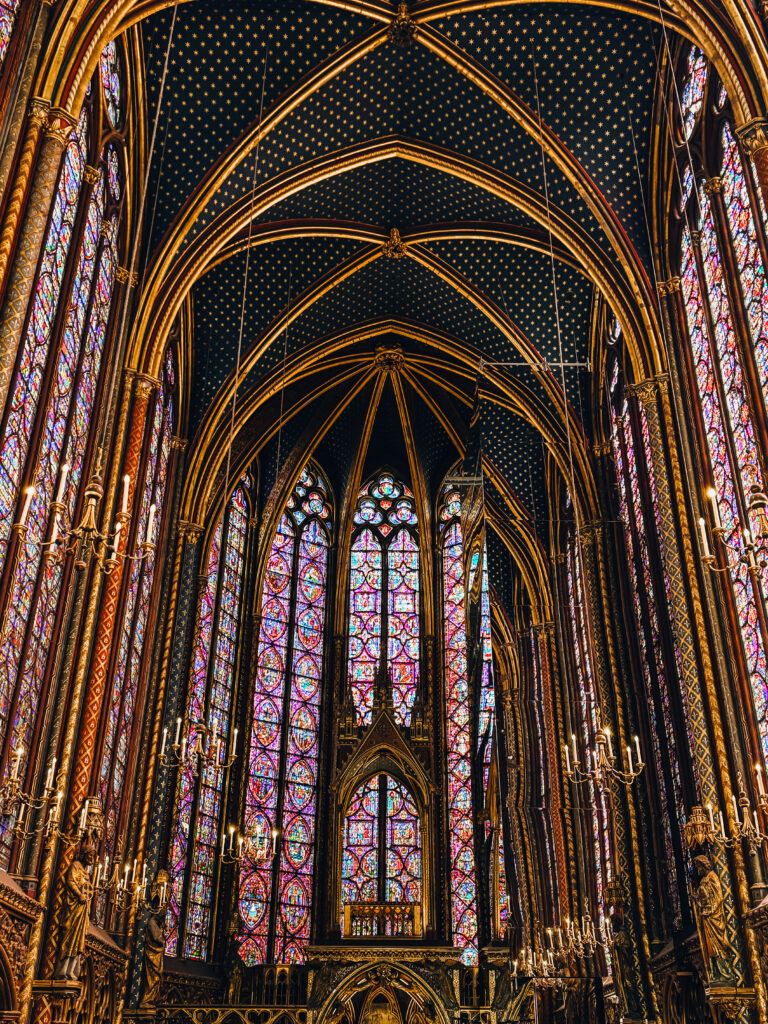 A breathtaking Gothic chapel interior featuring soaring stained glass windows, golden ribbed vaults, and a starry navy ceiling.