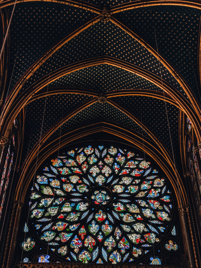 Close-up of the magnificent rose window with intricate stained glass depictions, framed by golden arches and a star-studded ceiling.