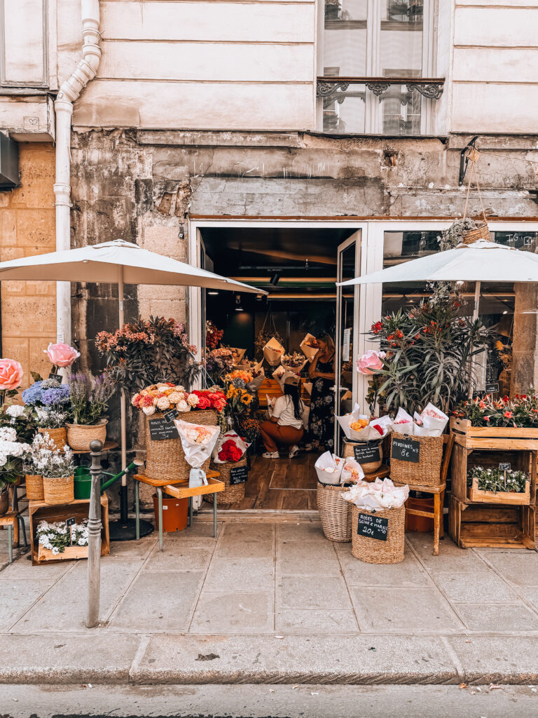 A charming flower boutique with colorful bouquets spilling onto the sidewalk, under white umbrellas and surrounded by rustic baskets and crates.