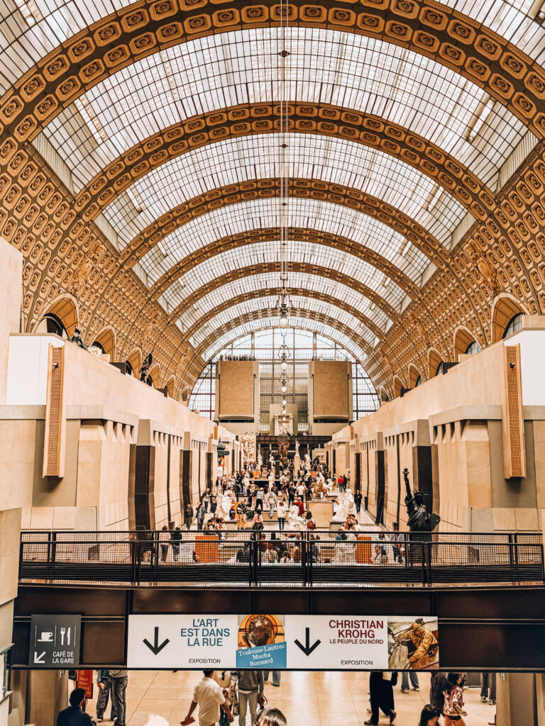 The central hall of Musée d'Orsay bustling with visitors beneath its iconic arched glass ceiling, once a former railway station.
