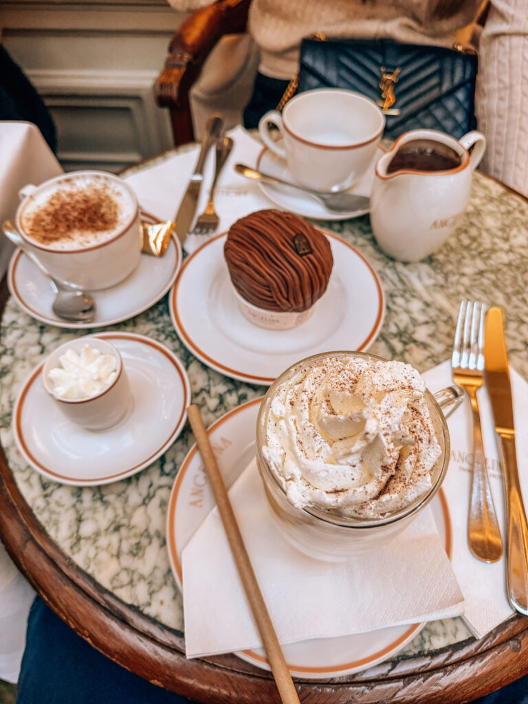 A marble café table set with a Mont Blanc dessert, rich hot chocolate, cappuccino, and whipped cream at the elegant Angelina tea salon.