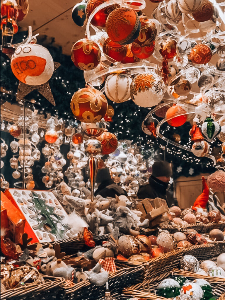 Close-up of a Christmas market stall in Vienna filled with handmade ornaments, glass baubles, and festive decorations, with warm lights and shoppers in the background.