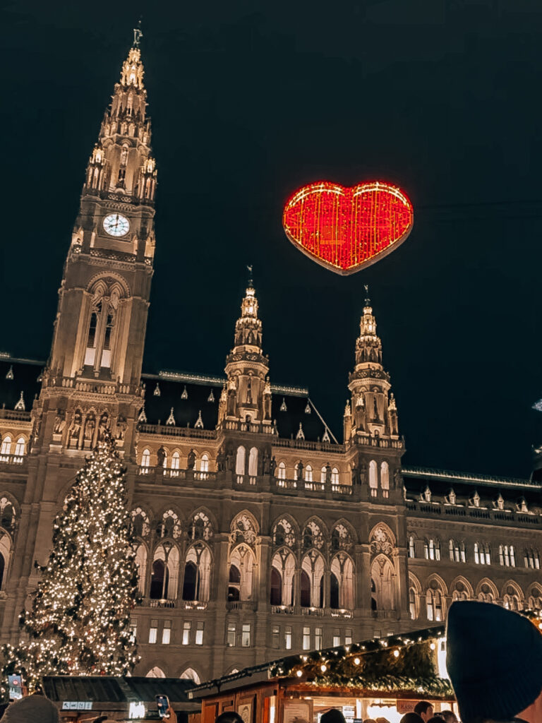 Vienna’s illuminated City Hall at night with a floating glowing red heart decoration and Christmas tree at the Rathausplatz Christmas Market.