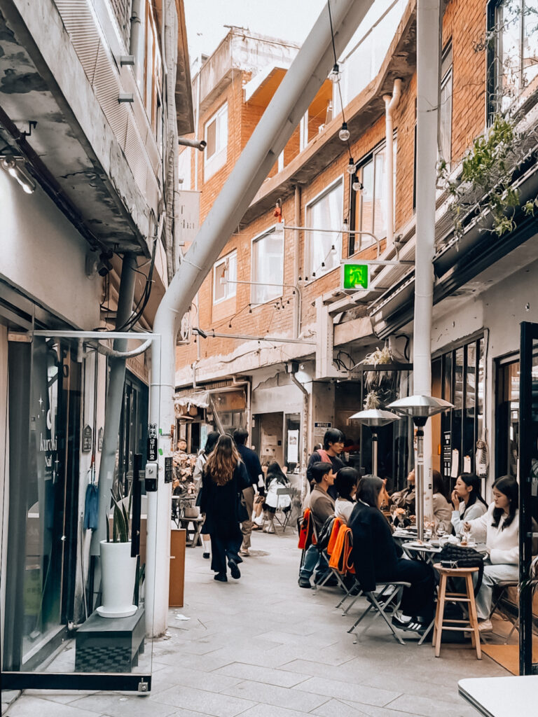 Narrow alley in Seoul lined with cafes and people dining outdoors on a crisp day, capturing the city's trendy and cozy vibe.