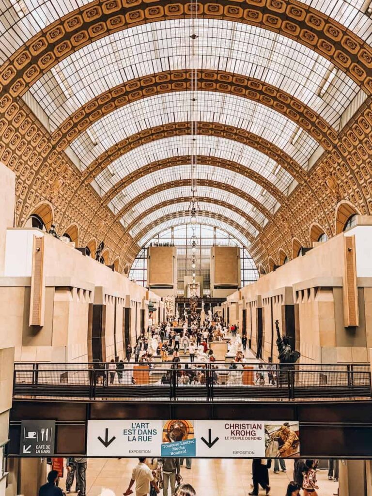 The central hall of Musée d'Orsay bustling with visitors beneath its iconic arched glass ceiling, once a former railway station.