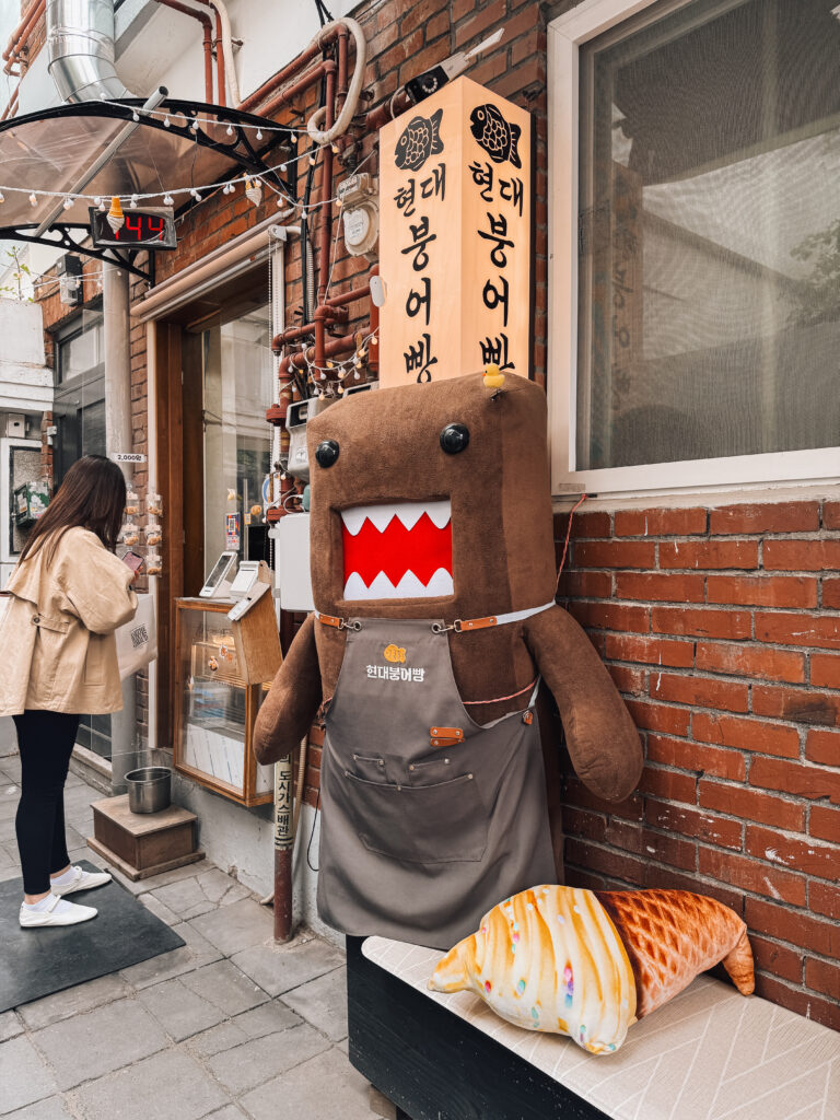 A quirky bungeoppang (fish-shaped pastry) shop in Seongsu-dong featuring a large Domo-kun character in an apron outside the storefront.