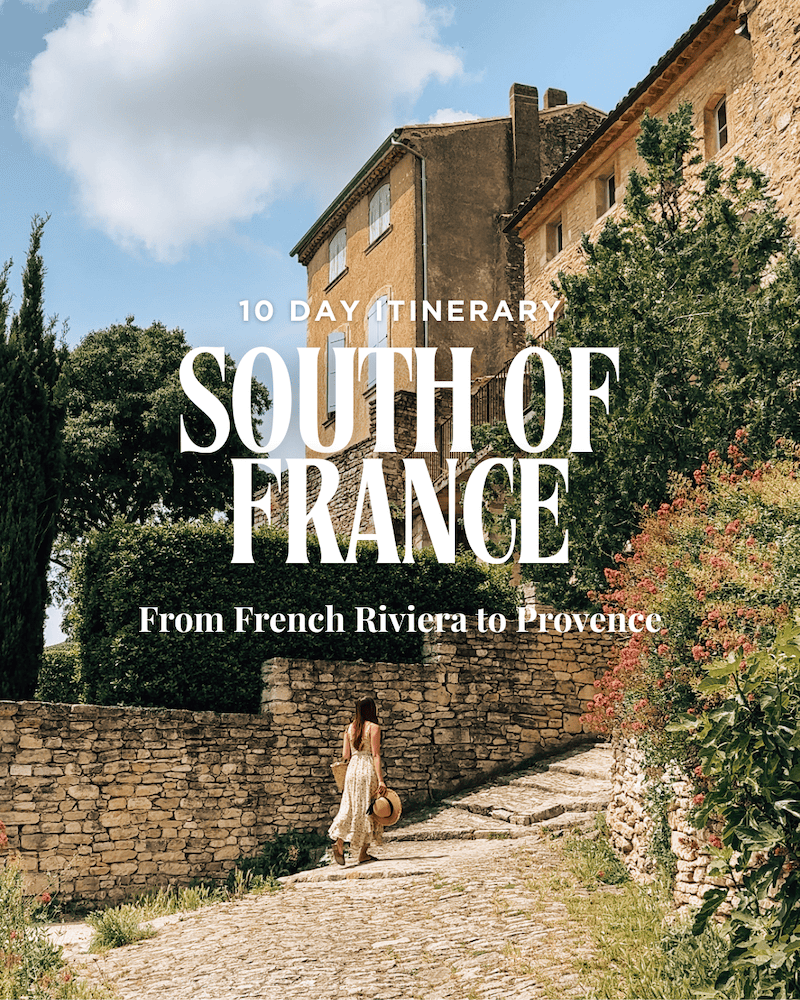 A woman in a flowy dress walks up a cobblestone street in a charming Provençal village, with warm stone houses and lush greenery surrounding her. Text overlay reads: “10 Day Itinerary – South of France – From French Riviera to Provence.”
