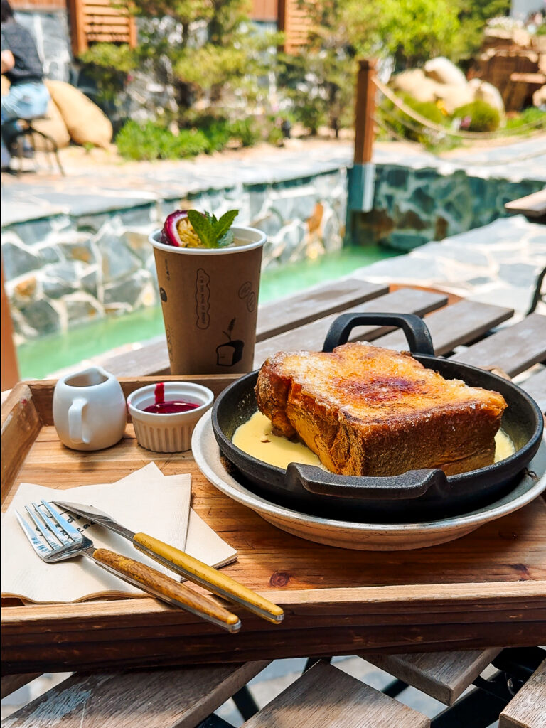 Thick-cut brioche French toast at Standard Bread in Seongsu, served in a skillet with fruit tea, raspberry sauce, and a small syrup pitcher at an outdoor café table.