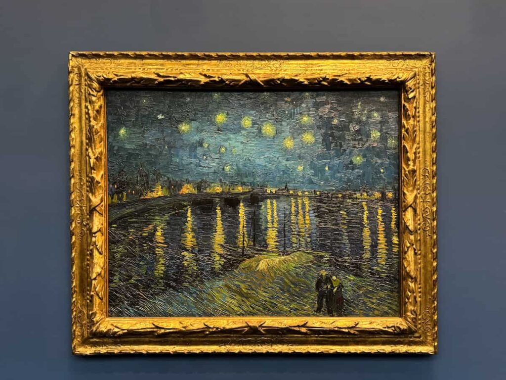 A framed oil painting of Van Gogh’s “Starry Night Over the Rhône” displayed on a navy blue wall, glowing with rich yellows and deep blues.