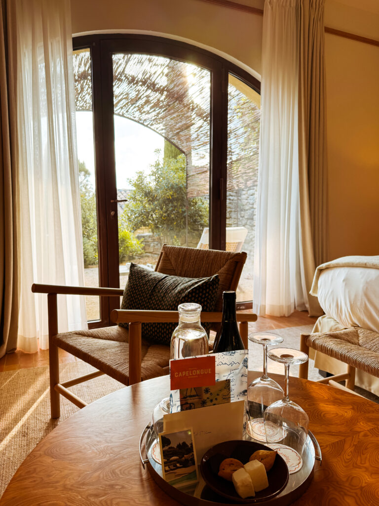 Table with a welcome tray featuring wine, water, and sweets inside a stylish Provençal hotel room.