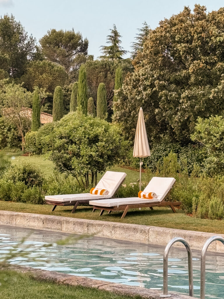 Two sun loungers with striped towels by a serene swimming pool, framed by cypress trees and Provençal greenery.