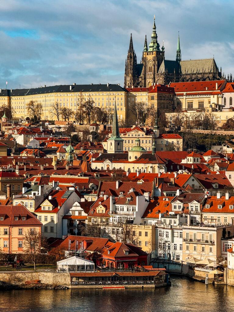 Scenic view of Prague Castle and St. Vitus Cathedral overlooking the red-roofed houses of Lesser Town (Malá Strana) across the Vltava River.