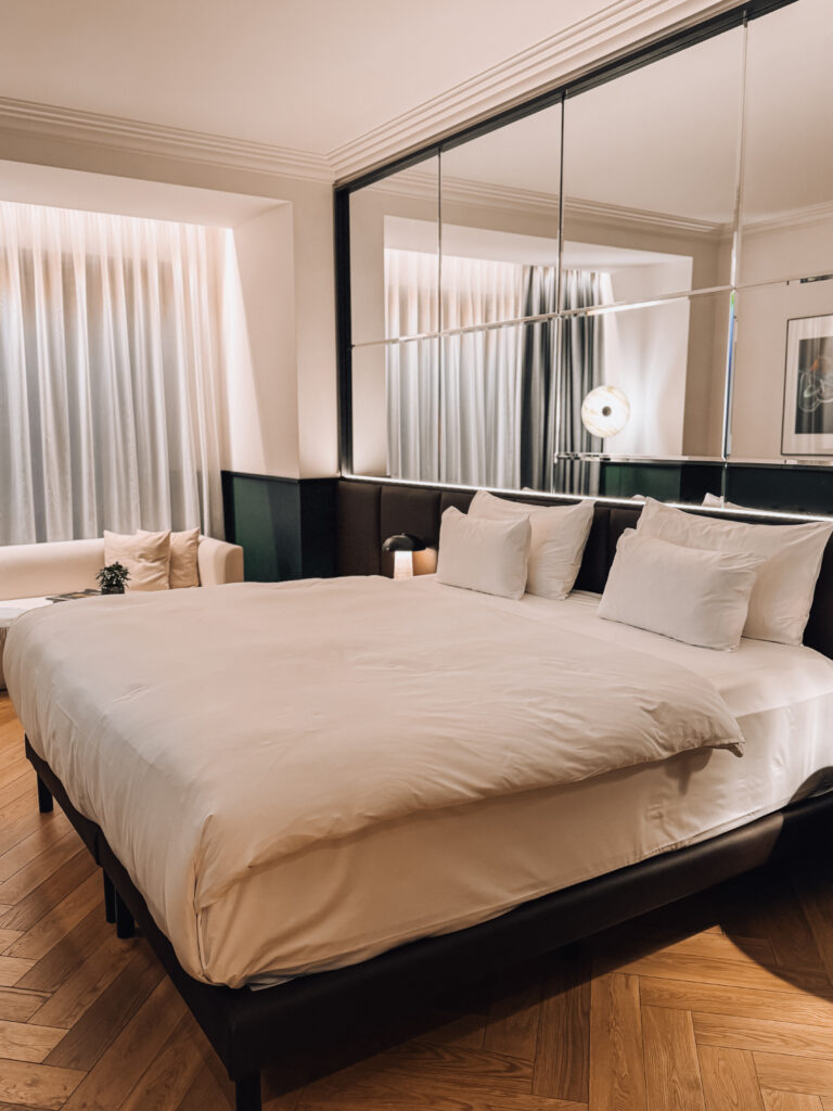 Modern and elegant hotel room at Almanac X Alcron Prague featuring a king-sized bed, warm lighting, parquet floors, and a mirrored headboard


