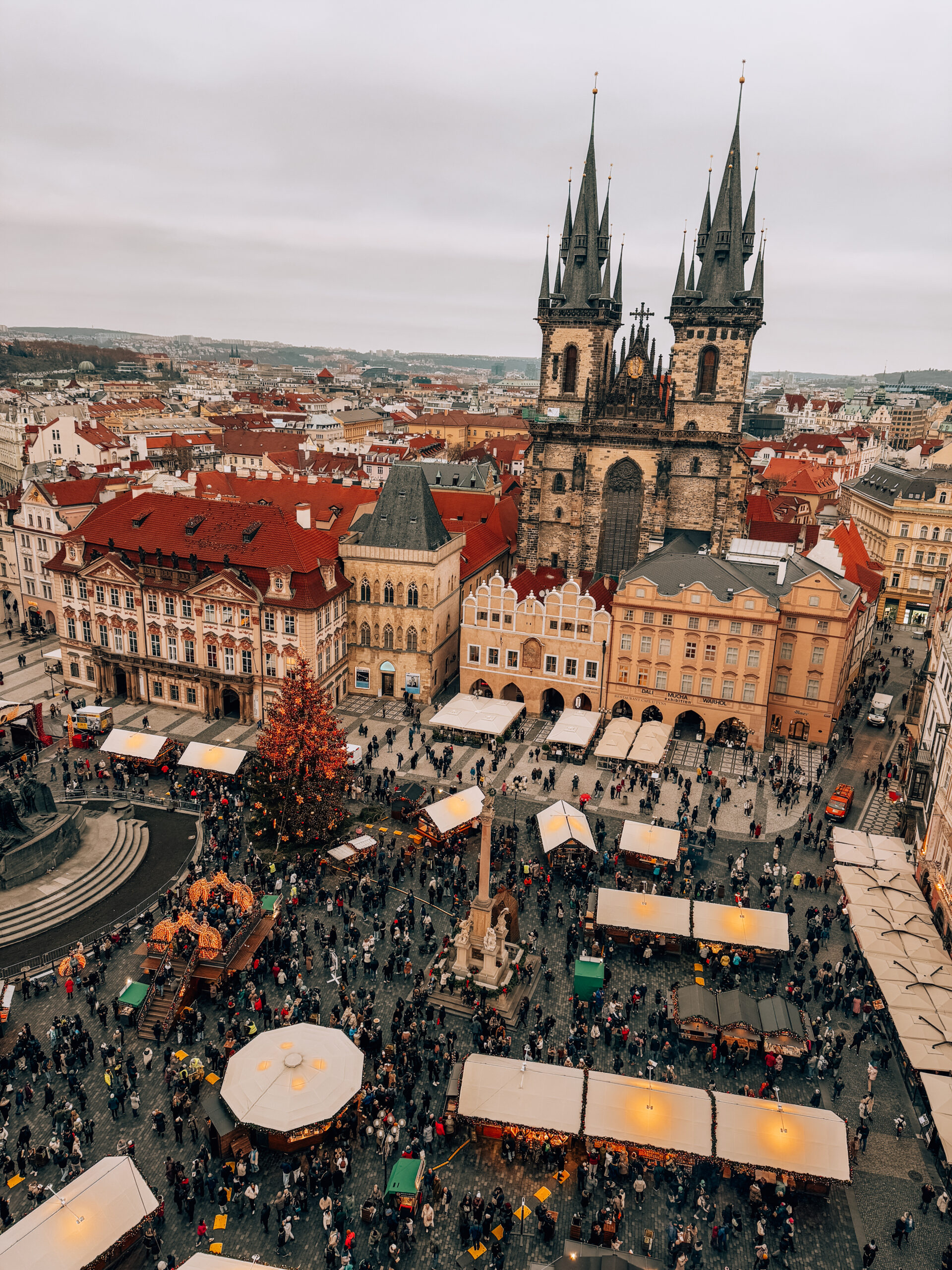 Bird’s-eye view of the Old Town Square Christmas Market in Prague with decorated stalls, a Christmas tree, and the Church of Our Lady before Týn in the background.