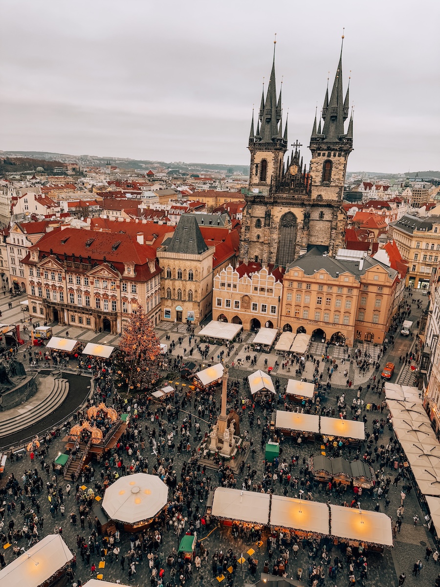 Bird’s-eye view of the Old Town Square Christmas Market in Prague with decorated stalls, a Christmas tree, and the Church of Our Lady before Týn in the background.