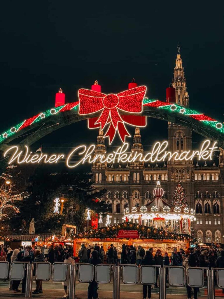 The brightly lit “Wiener Christkindlmarkt” arch and festive carousel at the Rathausplatz Christmas market in Vienna at night.