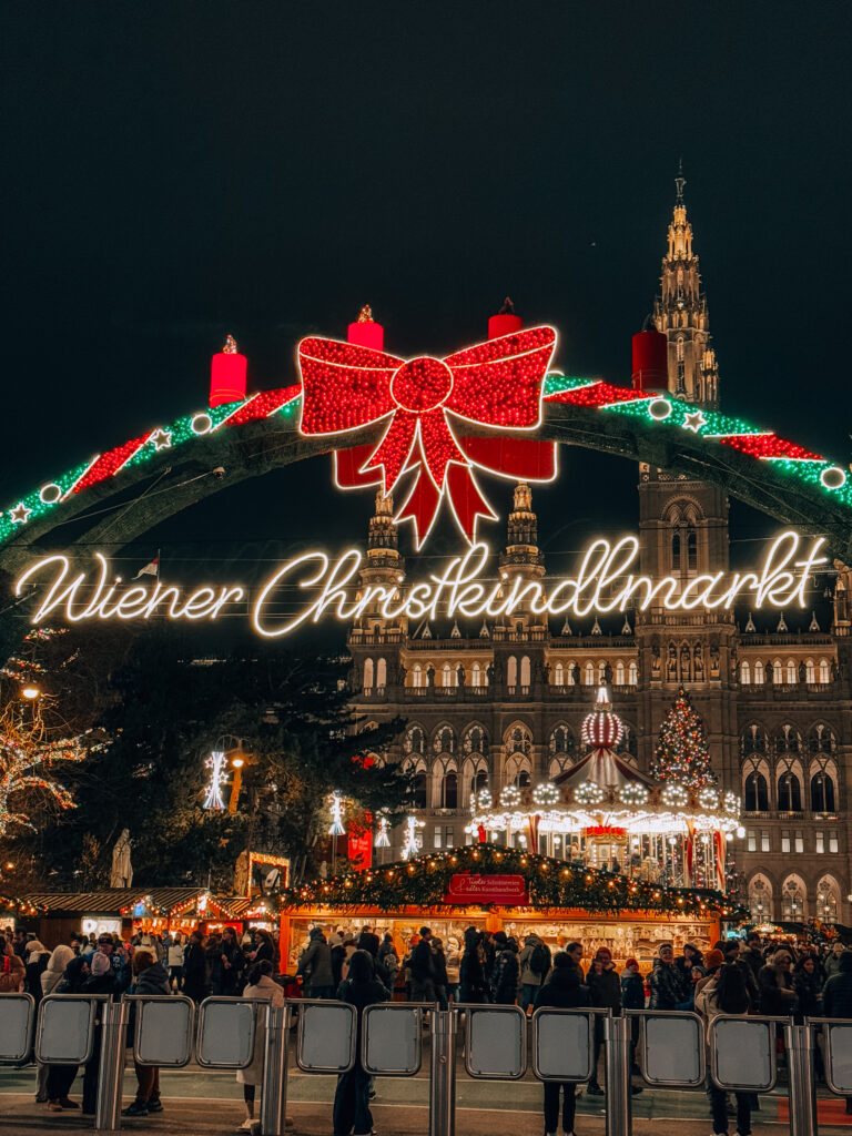 The brightly lit “Wiener Christkindlmarkt” arch and festive carousel at the Rathausplatz Christmas market in Vienna at night.