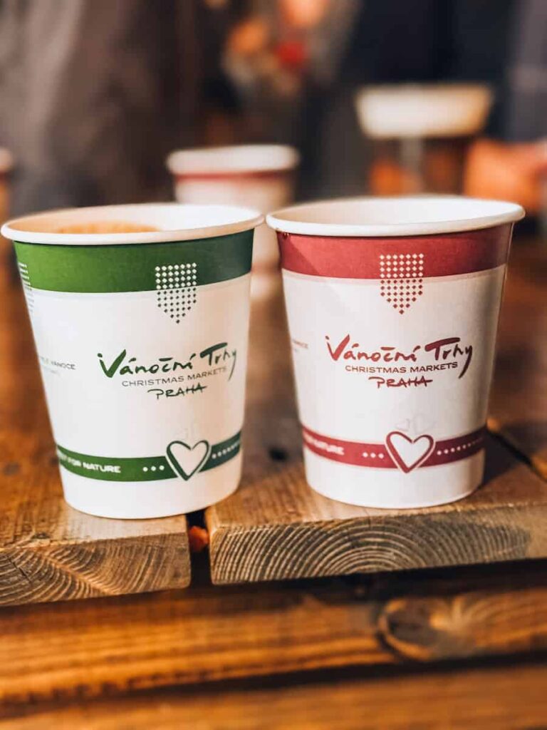 Two festive paper cups labeled “Vánoční Trhy Christmas Markets Praha” placed on a rustic wooden table, typically used for serving mulled wine or holiday drinks at Prague’s Christmas markets
