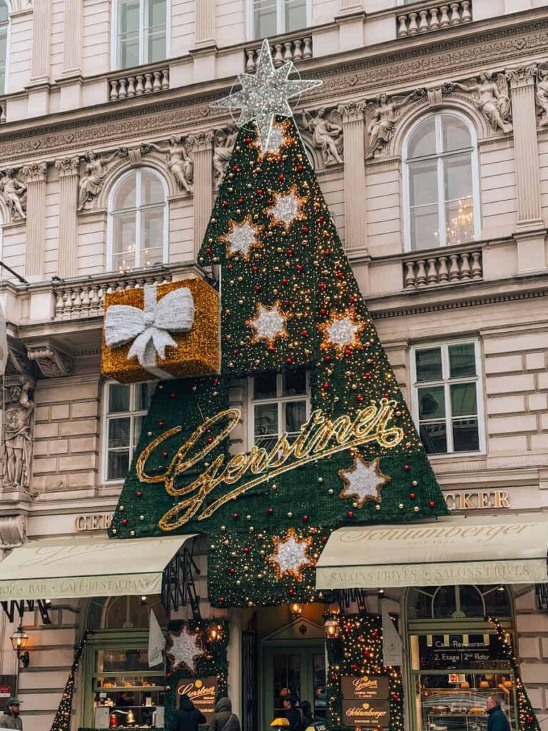 Festive Christmas tree-shaped decoration with sparkling stars and a gift box adorning the historic Gerstner Café-Restaurant façade in Vienna during the holiday season.