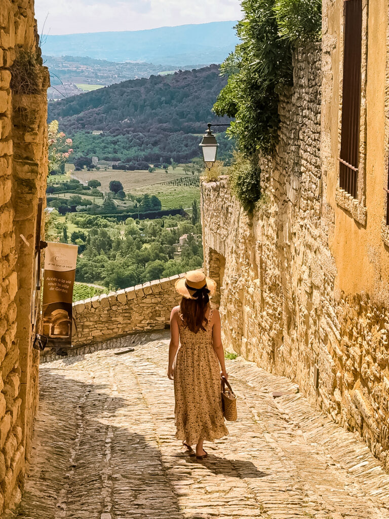 Traveler in a summer dress strolling down a steep cobbled lane with panoramic valley views in Gordes France. 