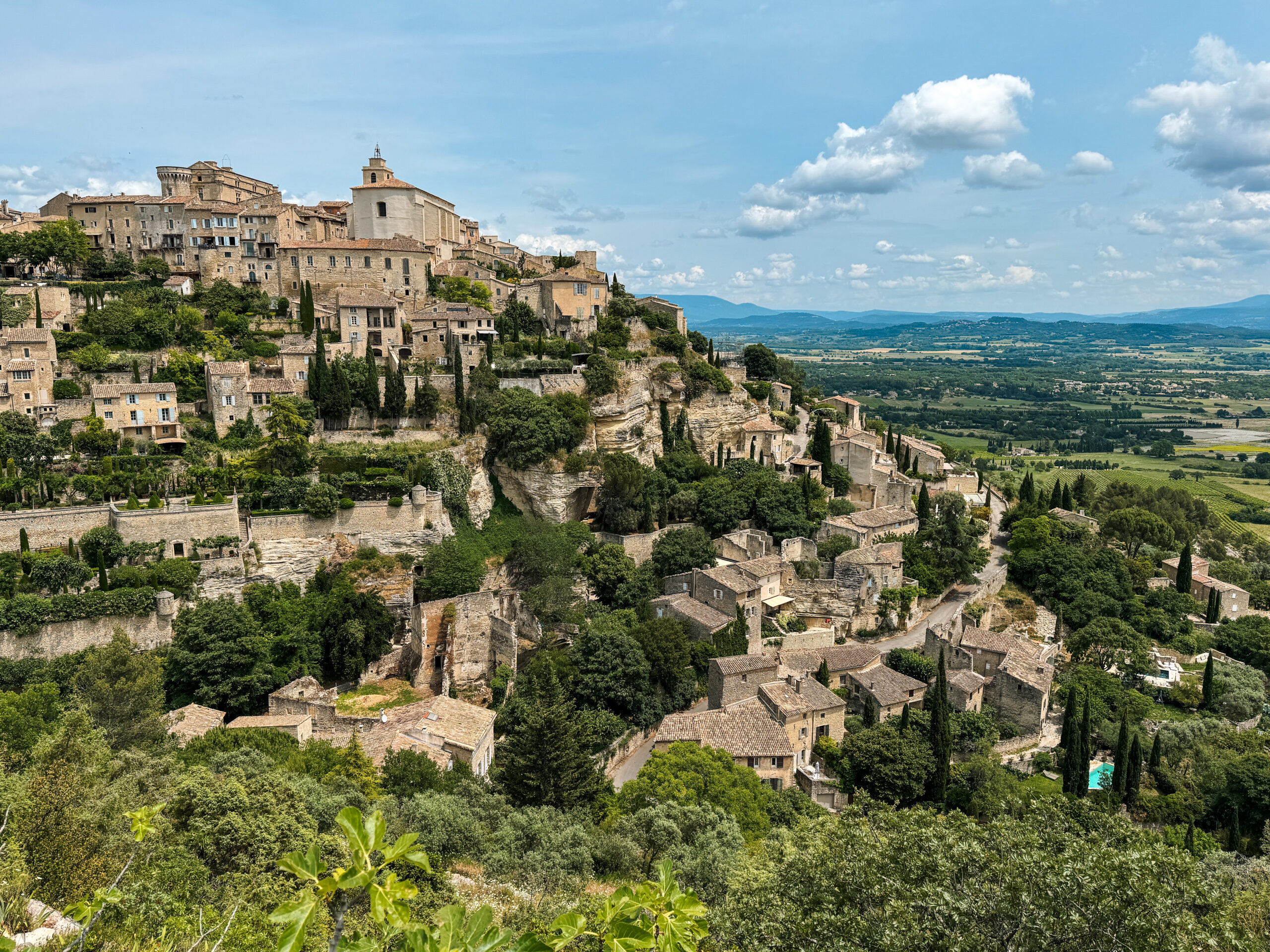 Hilltop stone village of Gordes cascading down a cliff with the Luberon Valley stretching into the distance.