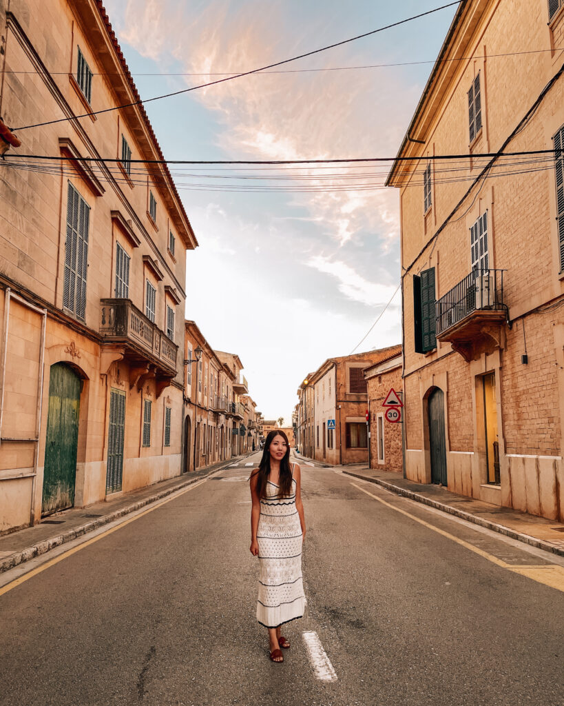 A woman wearing a striped crochet dress standing in the streets of Santanyi during her Mallorca itinerary