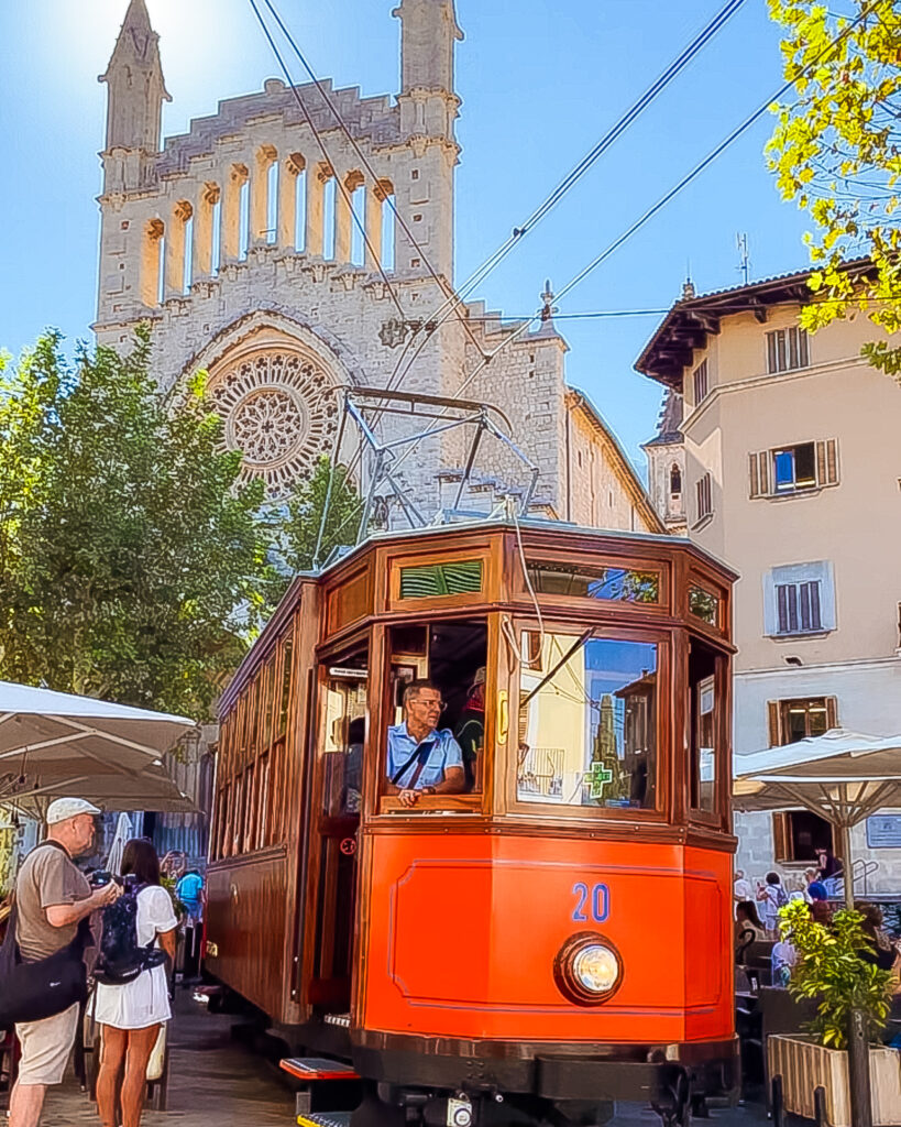 Historic wooden tram in Sóller passing through the town's main square with mountains in the background.