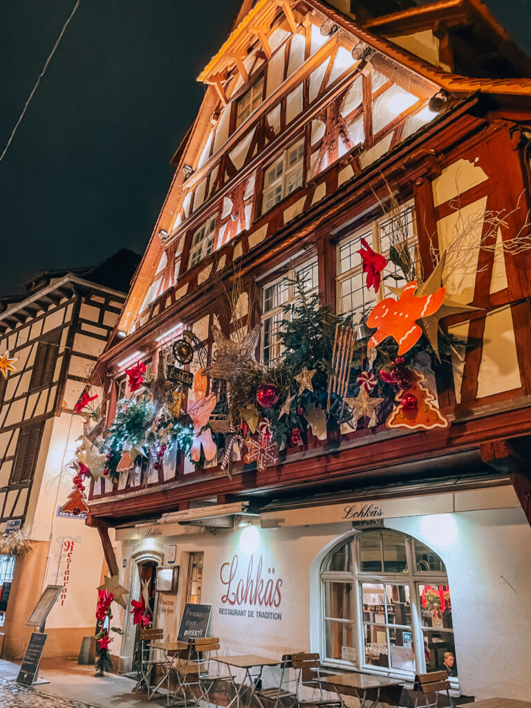 Alsatian half timbered house restaurant decorated with Christmas stars, gingerbread ornaments, and festive lights at night.