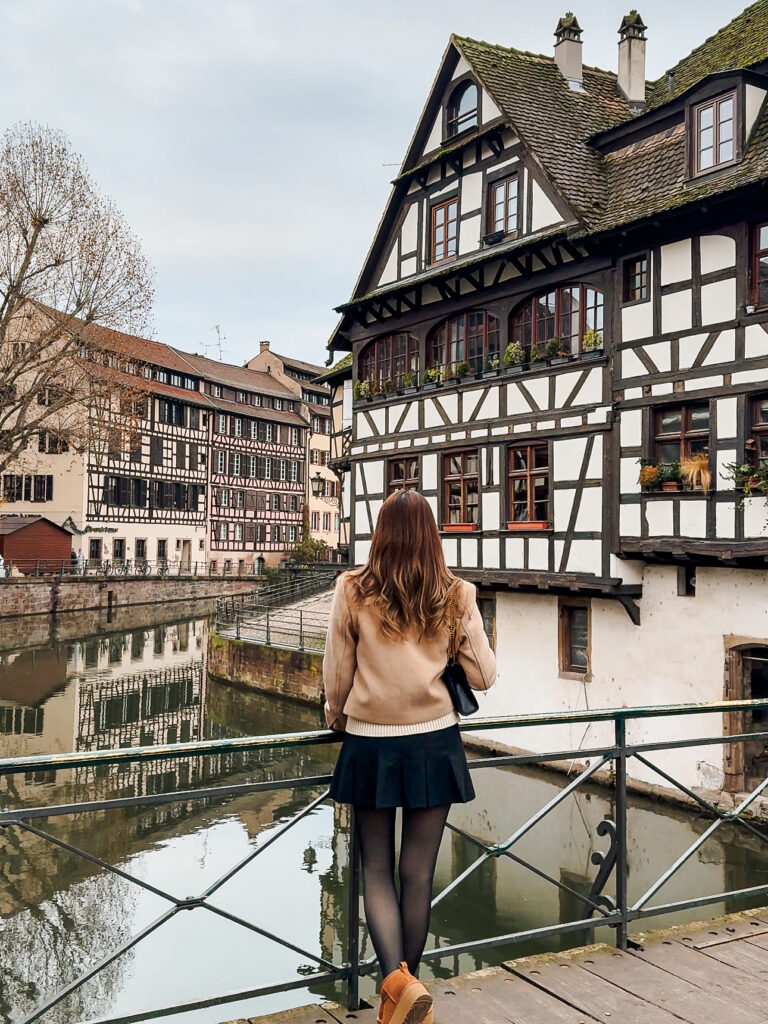 Traveler standing on a bridge overlooking half timbered houses and canals in Petite France, Strasbourg during winter.