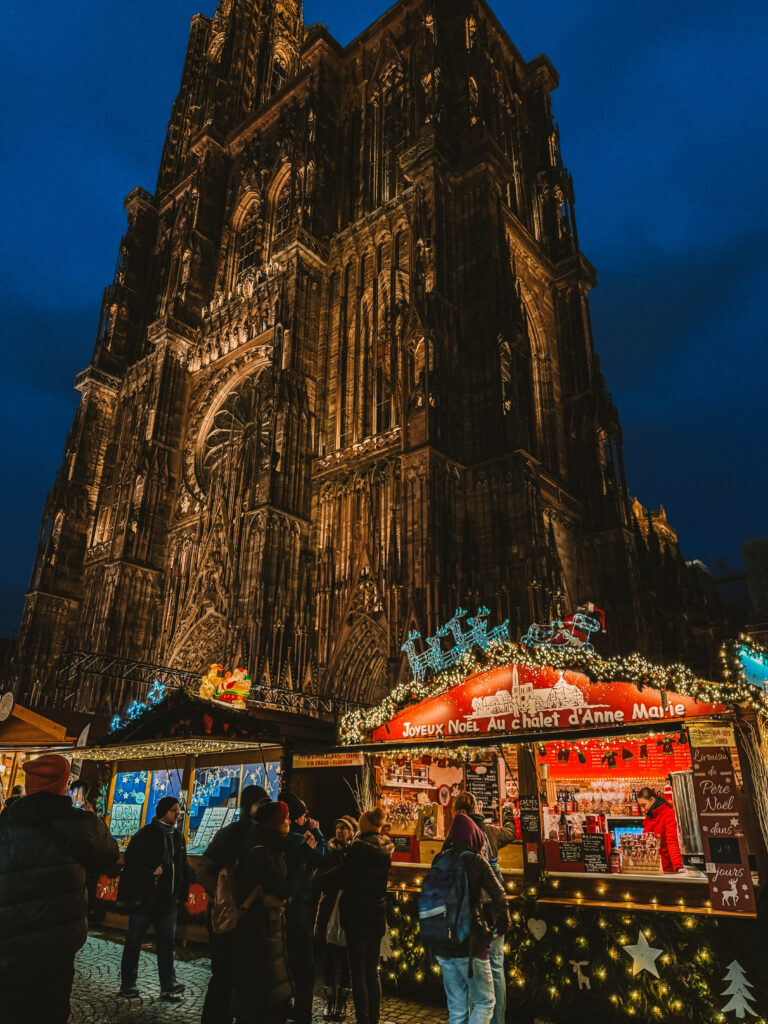 Strasbourg Cathedral illuminated against the night sky with Strasbourg Christmas market stalls glowing in the square.