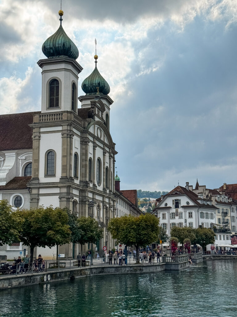 The twin green domes of Lucerne’s Jesuit Church rising above the Reuss River promenade.
