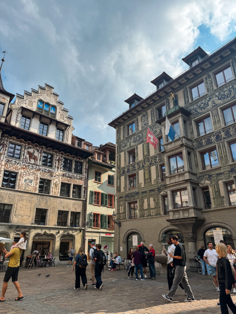 A lively square with frescoed buildings and people strolling through the cobblestones.