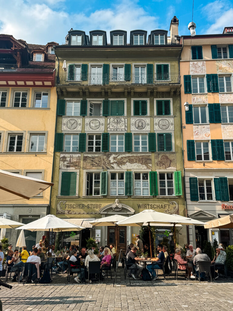 A busy restaurant terrace with umbrellas set against colorful, historic façades.