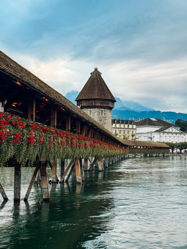 Covered wooden bridge lined with vibrant red flowers, leading toward the Water Tower.
